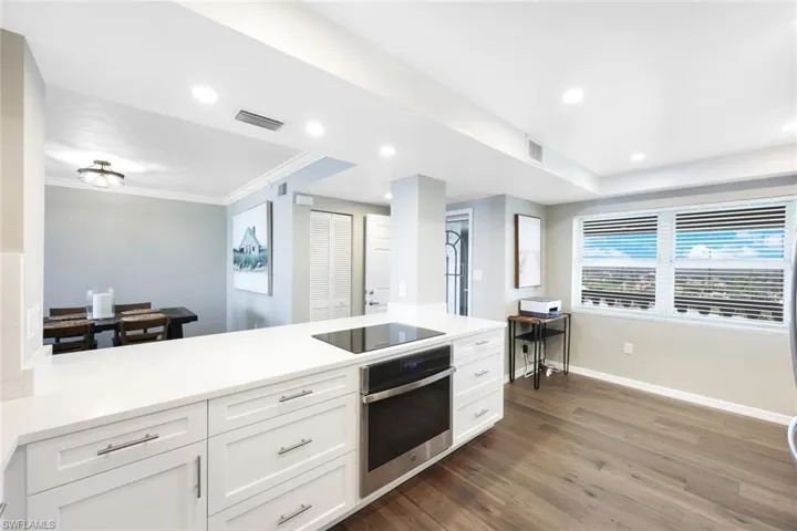 Kitchen featuring stainless steel oven, black electric cooktop, white cabinetry, hardwood / wood-style flooring, and ornamental molding