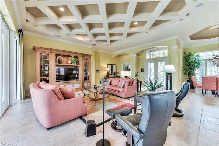 Living room featuring beamed ceiling, ornate columns, light tile patterned flooring, ornamental molding, and coffered ceiling