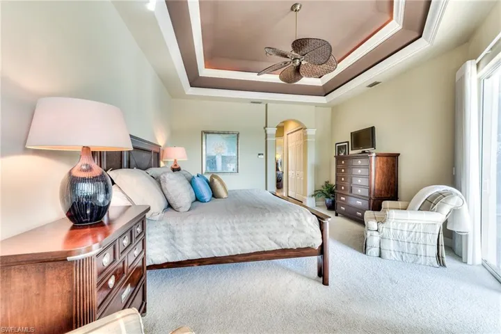 Bedroom featuring ornamental molding, ceiling fan, a tray ceiling, and carpet flooring