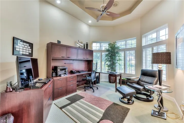 Carpeted office space with a towering ceiling, a raised ceiling, and ceiling fan
