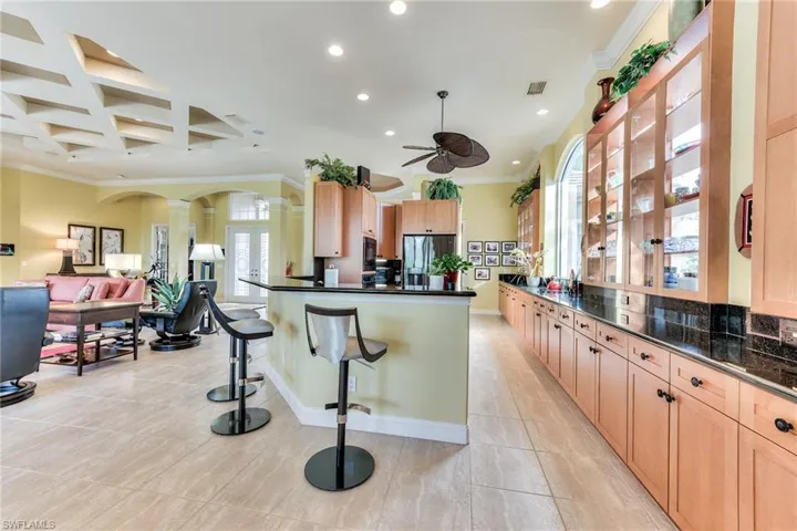 Kitchen featuring stainless steel fridge, ornate columns, a kitchen bar, crown molding, and ceiling fan