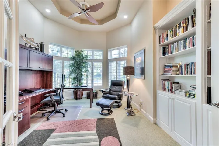Carpeted home office featuring a high ceiling, a raised ceiling, ceiling fan, and built in features