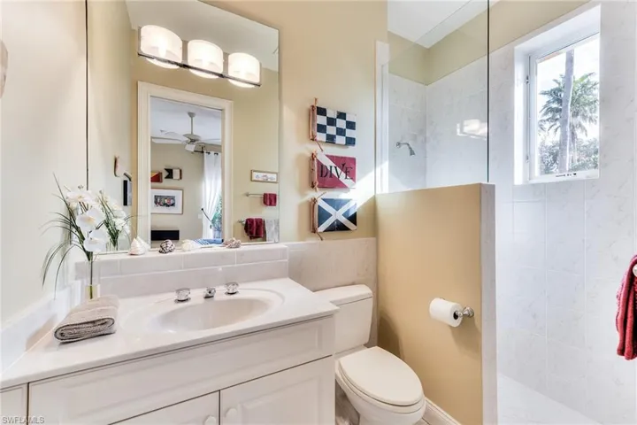 Bathroom featuring ceiling fan, a tile shower, vanity, and toilet