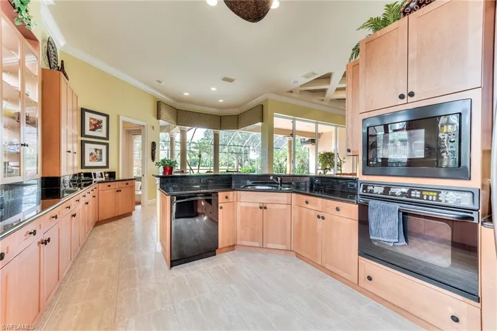 Kitchen with black appliances, light brown cabinetry, crown molding, and kitchen peninsula