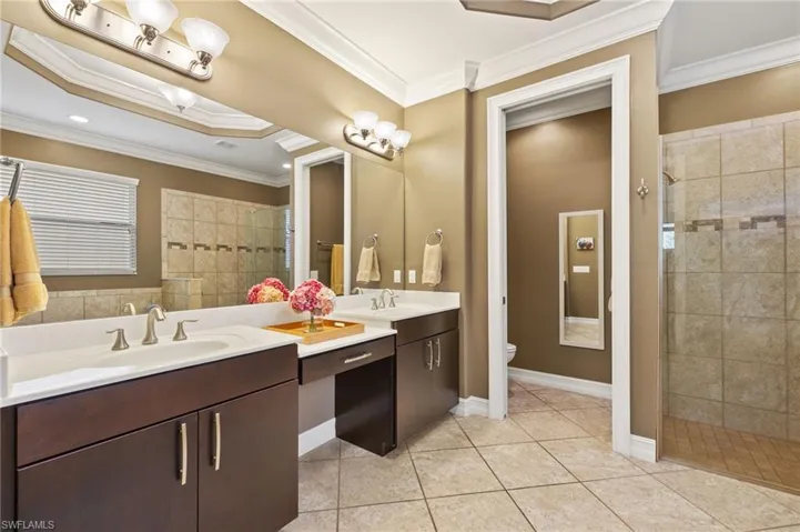 Bathroom with crown molding, tiled shower, vanity, tile patterned floors, and toilet