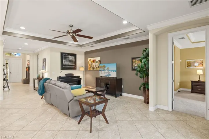 Living room with crown molding, ceiling fan, a tray ceiling, and light tile patterned flooring