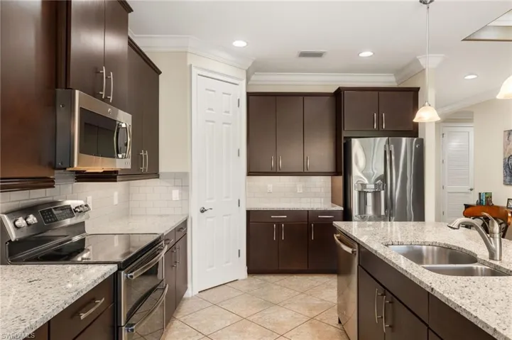 Kitchen with pendant lighting, sink, dark brown cabinets, stainless steel appliances, and decorative backsplash