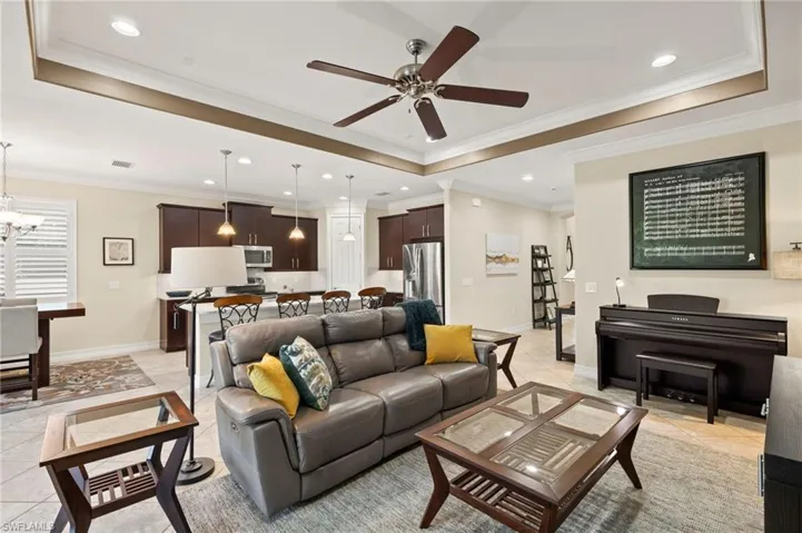 Living room with crown molding, a tray ceiling, ceiling fan with notable chandelier, and light tile patterned floors