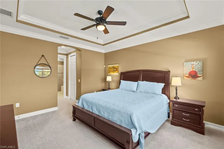 Bedroom featuring a raised ceiling, crown molding, light carpet, and ceiling fan