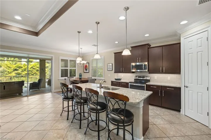 Kitchen with pendant lighting, sink, appliances with stainless steel finishes, a kitchen island with sink, and dark brown cabinets