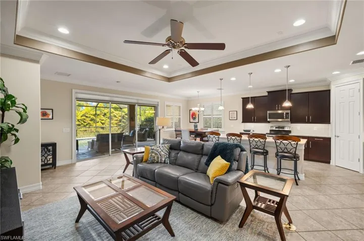 Living room with light tile patterned floors, crown molding, a raised ceiling, and ceiling fan