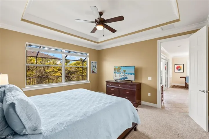 Carpeted bedroom with crown molding, a raised ceiling, and ceiling fan