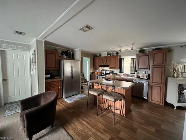 Kitchen featuring a kitchen breakfast bar, rail lighting, dark wood-type flooring, a kitchen island, and stainless steel appliances