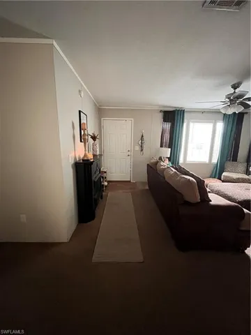 Carpeted entryway of living room with ceiling fan and ornamental molding