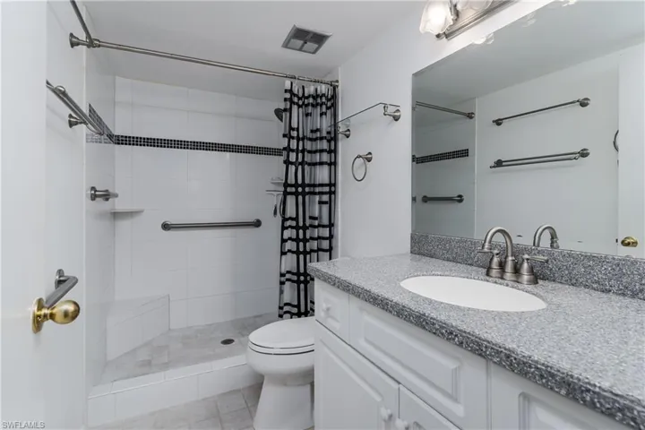 Bathroom featuring a tile shower, toilet, vanity, and visible vents