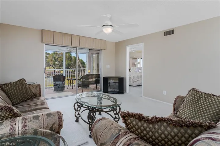 Carpeted living room featuring visible vents, baseboards, and ceiling fan
