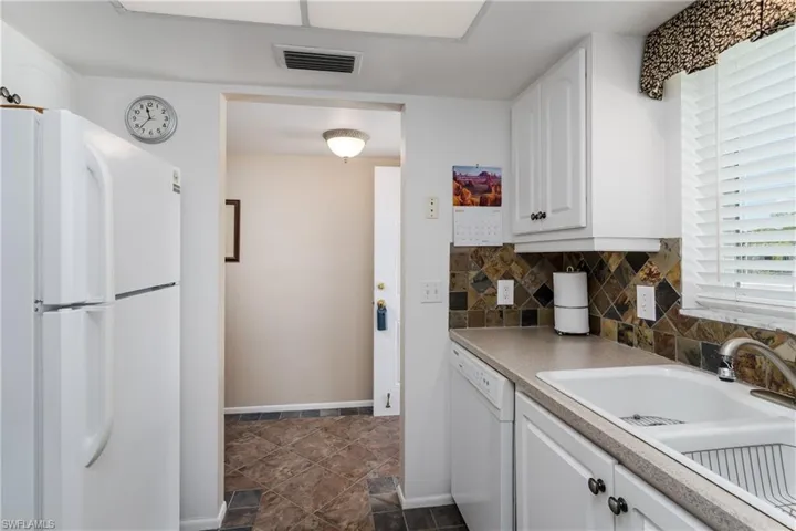 Kitchen with a sink, visible vents, backsplash, white cabinetry, and white appliances