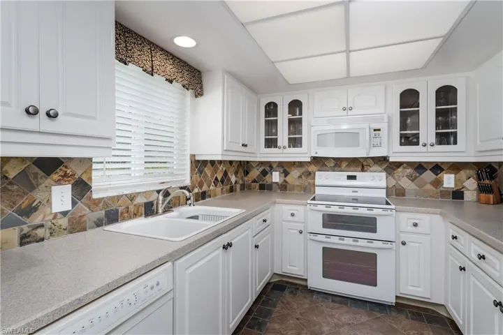Kitchen with white cabinetry, a sink, white appliances, and glass insert cabinets