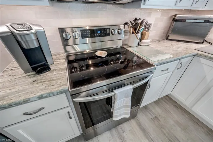 Kitchen featuring tasteful backsplash, white cabinetry, light stone counters, light wood-type flooring, and stainless steel electric range