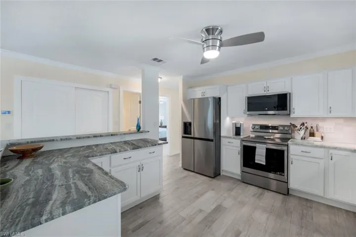 Kitchen with backsplash, stainless steel appliances, light hardwood / wood-style floors, white cabinets, and stone countertops