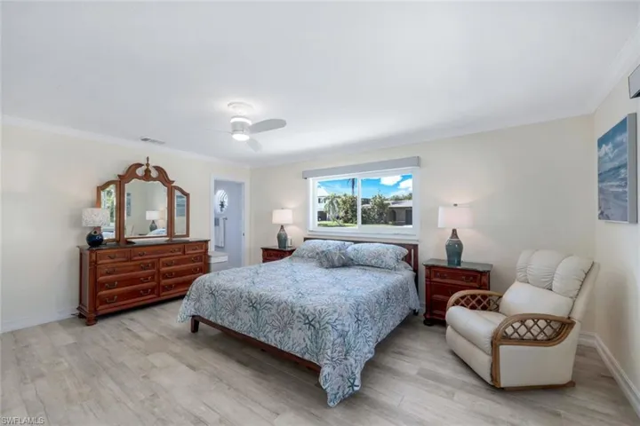 Bedroom with ensuite bath, ornamental molding, ceiling fan, and light wood-type flooring