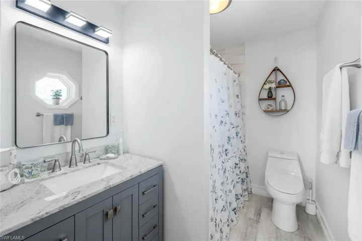 Bathroom with a shower with curtain, vanity, wood-type flooring, and toilet