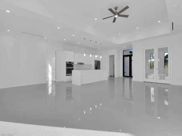 Unfurnished living room with french doors, light tile patterned floors, a raised ceiling, and ceiling fan