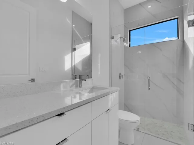 Bathroom featuring a shower with door, vanity, and toilet