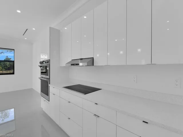 Kitchen with black electric cooktop, white cabinetry, stainless steel double oven, and light stone counters