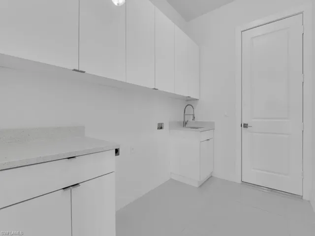 Washroom with electric dryer hookup, cabinets, sink, hookup for a washing machine, and light tile patterned floors.