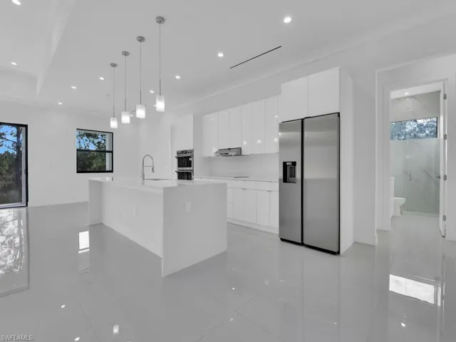 Kitchen with sink, hanging light fixtures, stainless steel appliances, a kitchen island with sink, and white cabinets