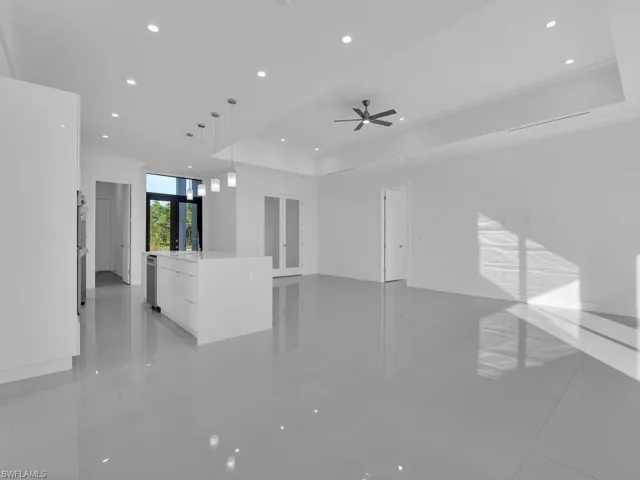 Unfurnished living room with french doors, a tray ceiling, light tile patterned floors, and ceiling fan