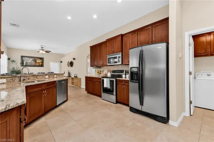Kitchen featuring granite countertops, wood cabinetry, stainless steel appliances, and tile flooring