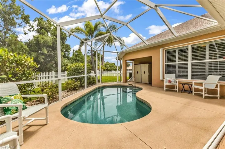 Screened-in patio with an irregular-shaped pool, concrete decking, an exterior door, exterior windows with horizontal blinds, and a white picket fence