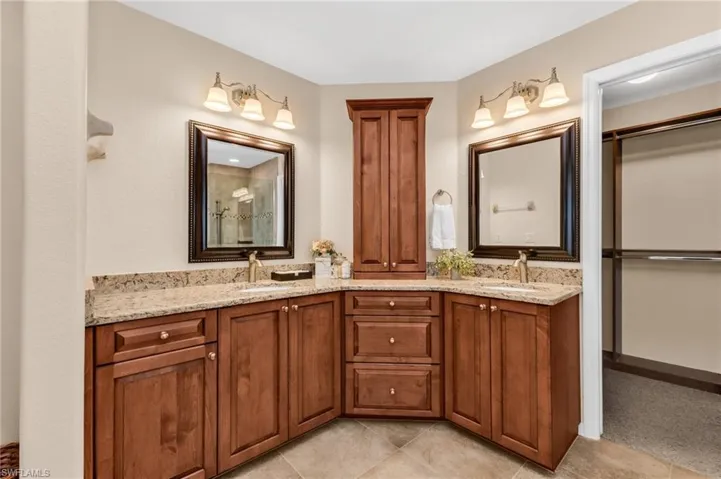 Bathroom featuring dual sink vanities with granite countertops, wood cabinetry, and framed mirrors