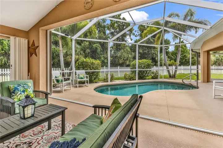 Screened lanai featuring a free-form swimming pool with a handrail, a concrete pool deck, and a white picket fence