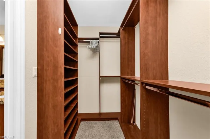 Walk-in closet featuring built-in wood-finish shelving, multiple hanging rods, and light beige wall paint