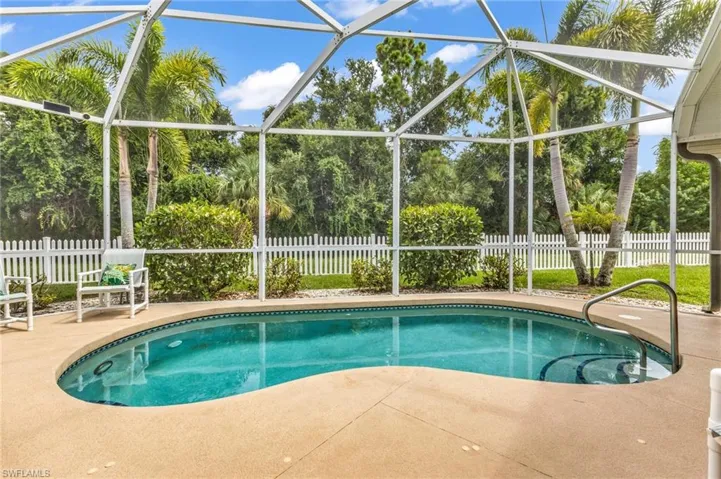 Outdoor pool area featuring a freeform pool, concrete deck, and a screened enclosure