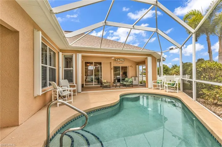 Screened-in outdoor living space featuring a free-form pool with integrated steps and a deck-mounted handrail