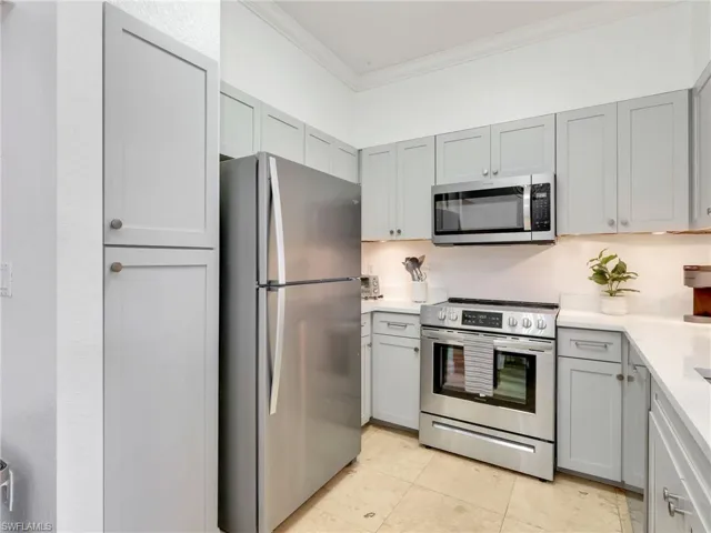 Kitchen featuring gray cabinets, stainless steel appliances, crown molding, light stone counters, and light tile patterned floors