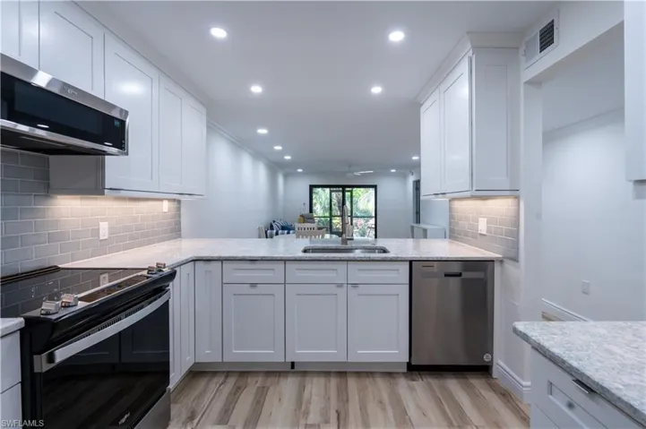 Kitchen featuring appliances with stainless steel finishes, white cabinetry, sink, kitchen peninsula, and light wood-type flooring