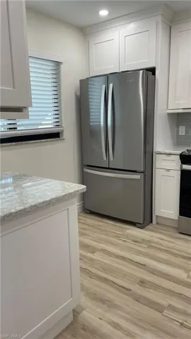 Kitchen featuring white cabinetry, stainless steel appliances, backsplash, light wood-type flooring, and light stone counters