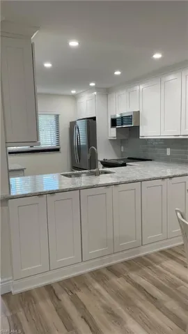 Kitchen featuring extractor fan, light wood-type flooring, stainless steel refrigerator, white cabinets, and light stone counters