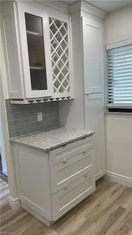 Bar featuring tasteful backsplash, light wood-type flooring, light stone countertops, and white cabinetry