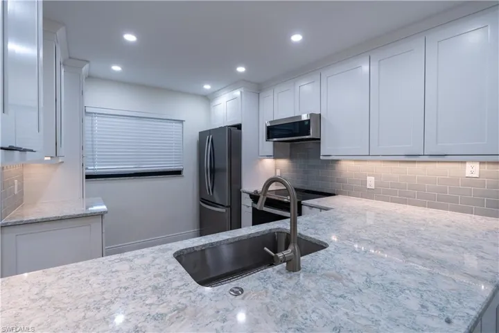 Kitchen with sink, appliances with stainless steel finishes, light stone counters, white cabinets, and decorative backsplash
