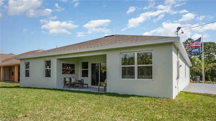 Rear view of house featuring stucco siding, a lawn, a patio, and a shingled roof