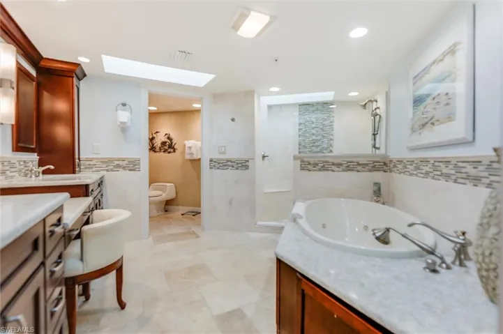 Bathroom with vanity, a tub with jets, walk in shower, tile walls, and a skylight