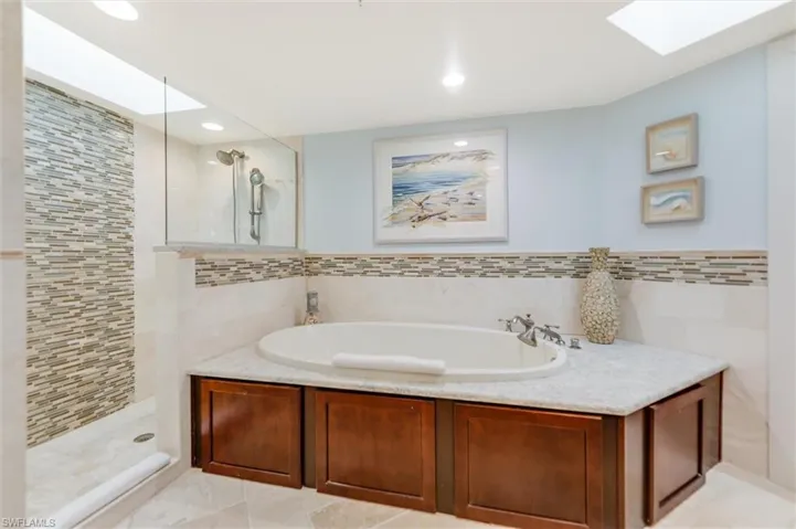 Bathroom with a walk in shower, a garden tub, tile walls, a skylight, and recessed lighting