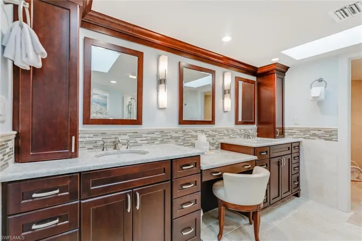 Bathroom featuring a skylight, double vanity, wainscoting, and tile walls