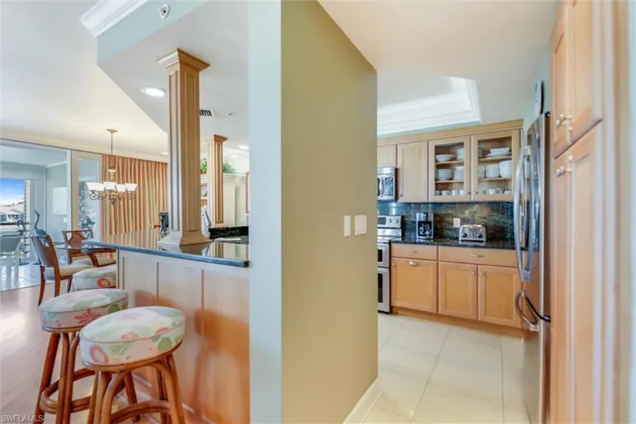 Kitchen featuring crown molding, glass fronted cabinets, stainless steel appliances, dark stone counters, and a kitchen bar